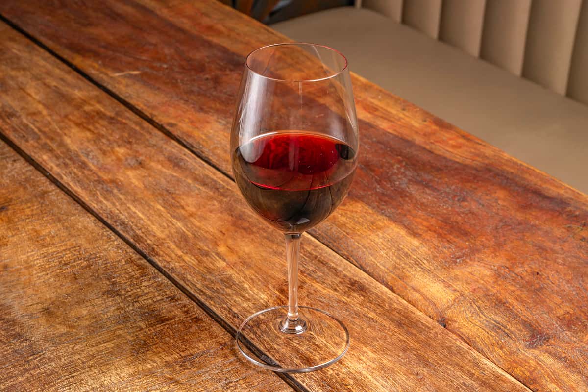 Deep red wine in a stemmed glass resting on a rustic wood table at The Downing Bottles and Bites.