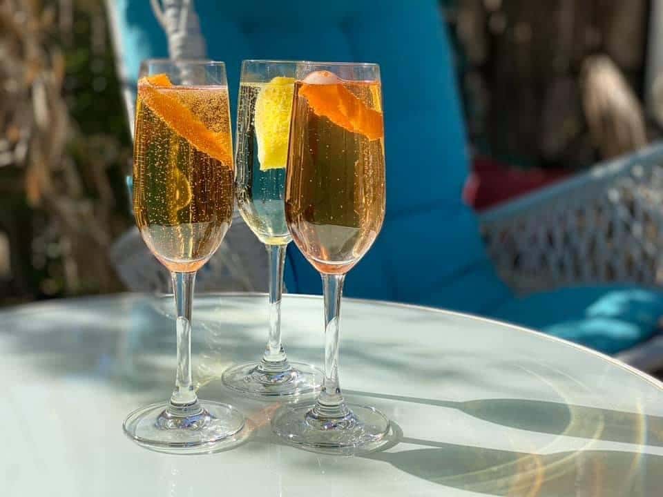 Trio of golden sparkling citrus cocktails garnished with orange peels on a white patio table at The Downing Bottles & Bites.