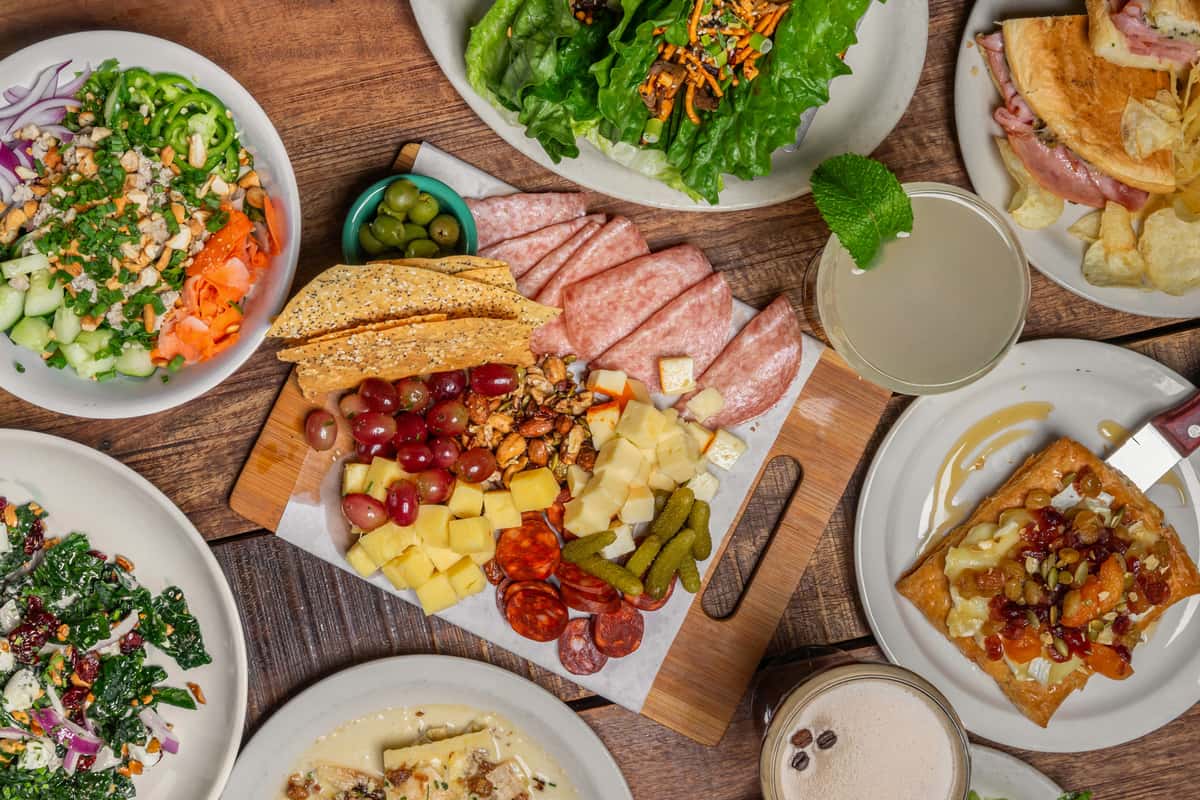 Overhead flat lay of a diverse gourmet spread featuring a central charcuterie board, various salads, appetizers, and cocktails from The Downing Bottles and Bites.