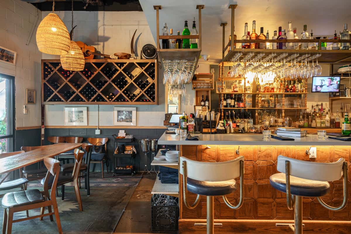 Warm, rustic bar interior of The Downing Bottles and Bites, showcasing a custom wine rack and illuminated liquor display.