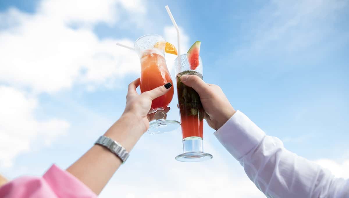 Friends raising colorful craft cocktails for a toast on the outdoor patio at a modern hotel restaurant and bar.
