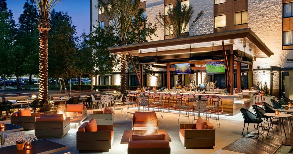 Outdoor hotel patio bar with fire pits, lounge seating, and open-air dining, creating a modern atmosphere for cocktails, happy hour, and evening gatherings.