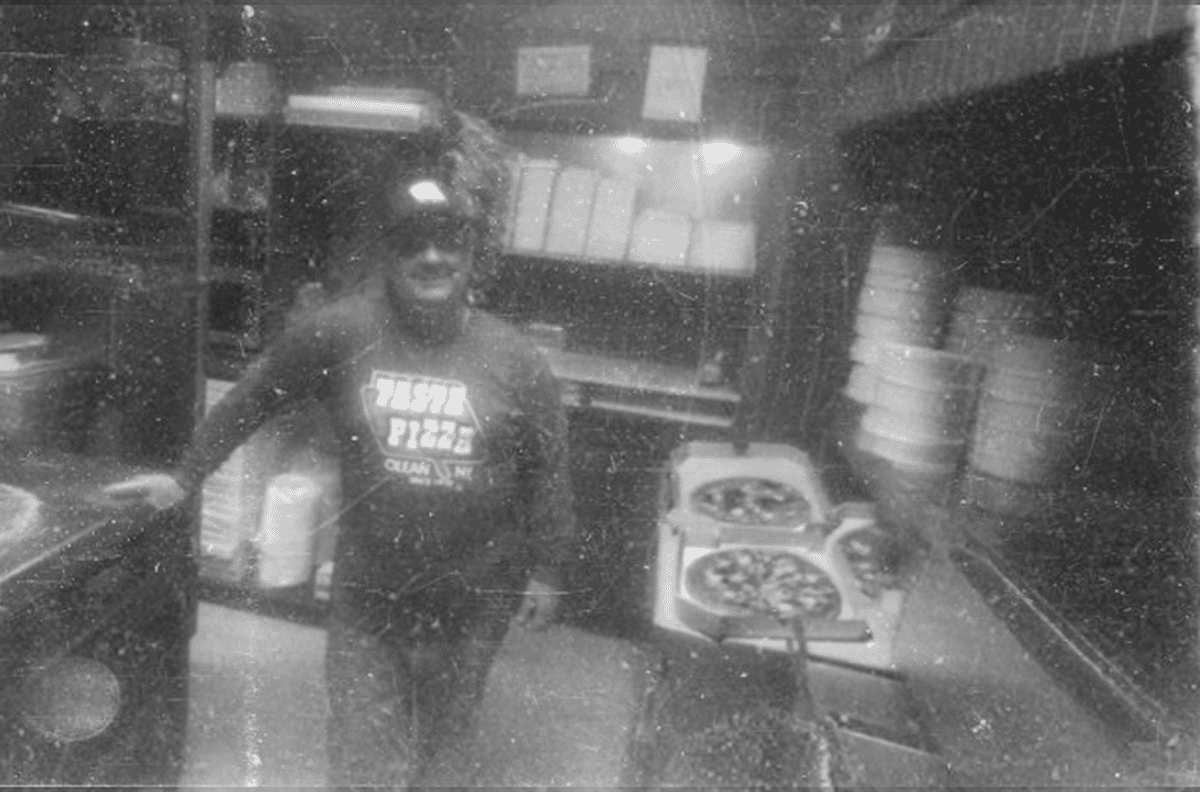 Owner standing in pizza kitchen with stacks of pizza
