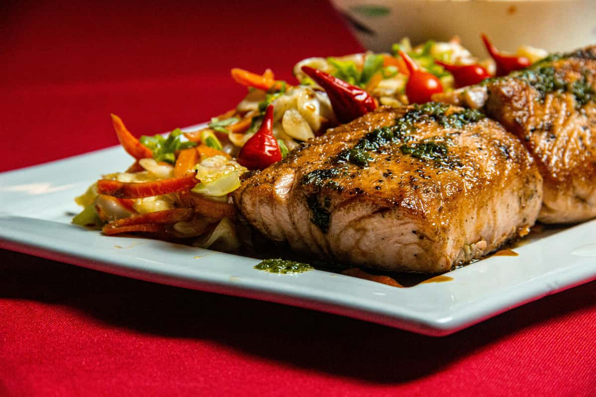 Grilled salmon fillets topped with a flavorful herb sauce, served with a vibrant salad of fresh cabbage, carrots, and chili peppers on a white plate.
