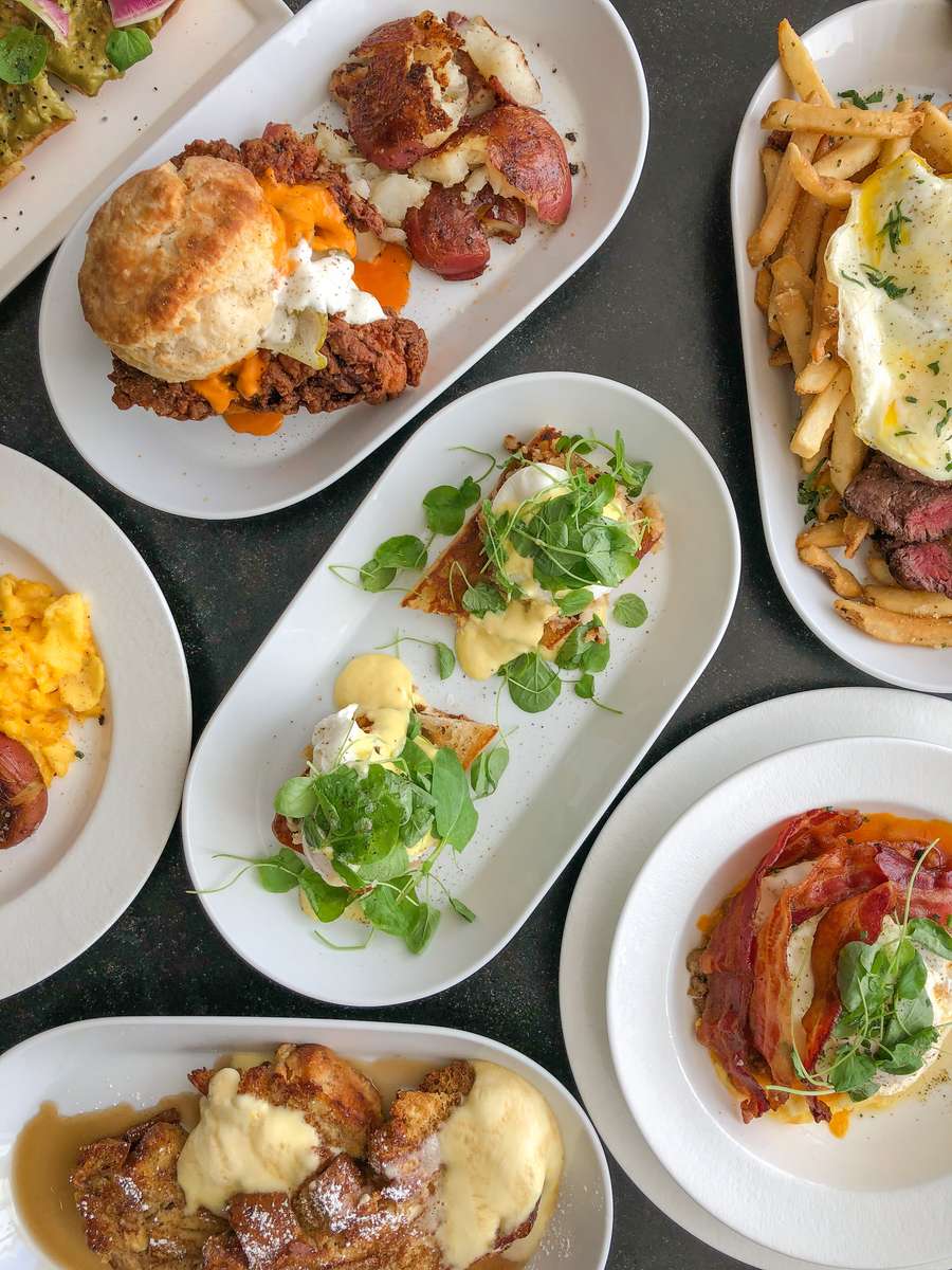 Tablescape with assorted brunch items - eggs benedict, pancakes, fried chicken biscuit