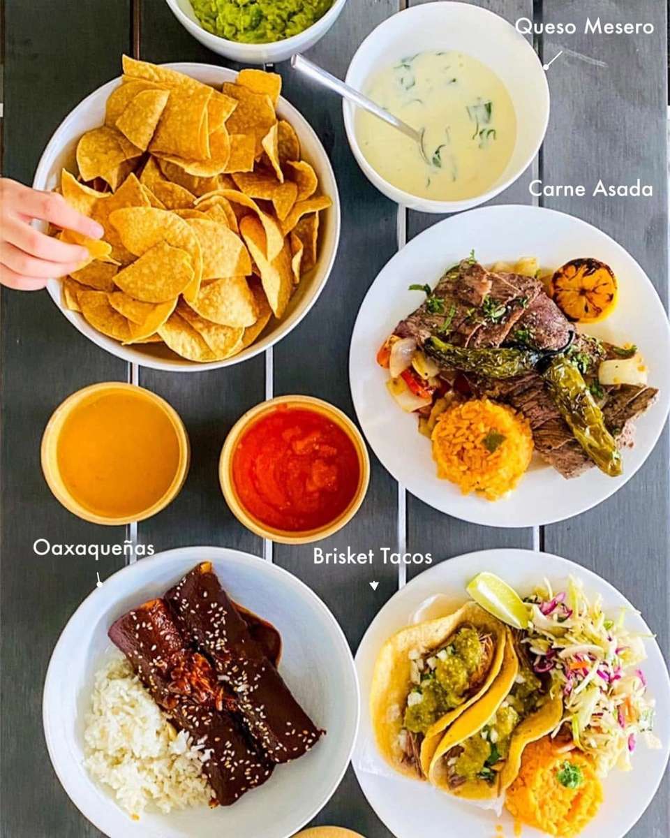 Mesero table spread with chips, queso, guacamole, tacos, carne asada, and Oaxaqueñas.