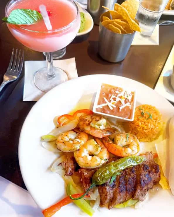 Mesero fajita plate with shrimp, steak, veggies, rice, beans, chips, and a pink margarita.