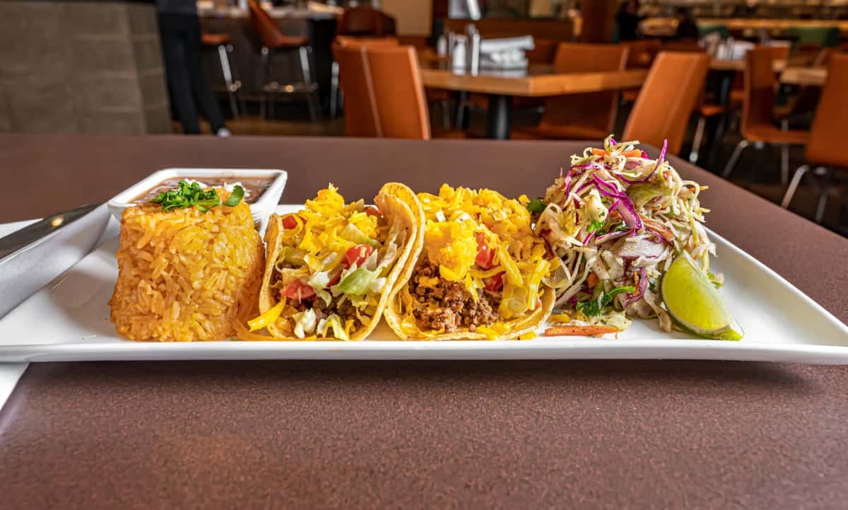 Mesero taco plate with seasoned tacos, rice, beans, and fresh slaw served in a warm and inviting dining setting.