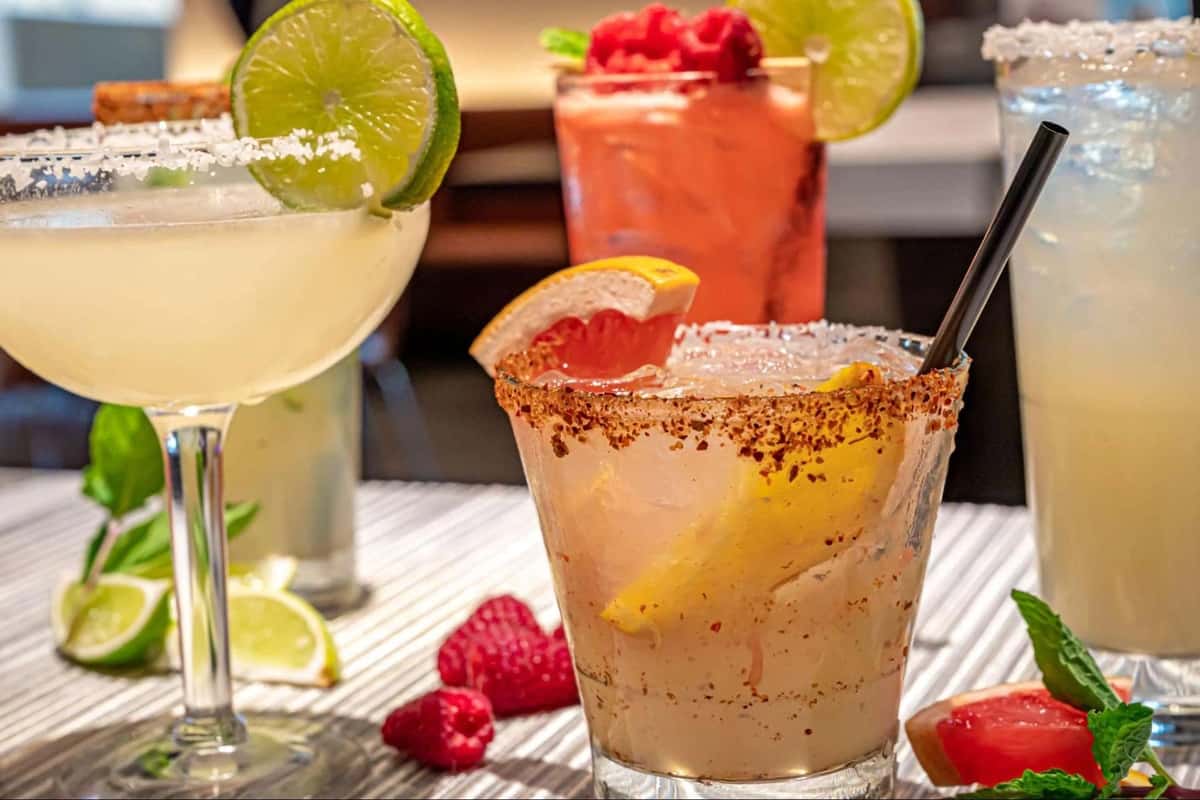 Colorful cocktails with citrus garnishes, spicy rims, and fresh berries arranged on a table.