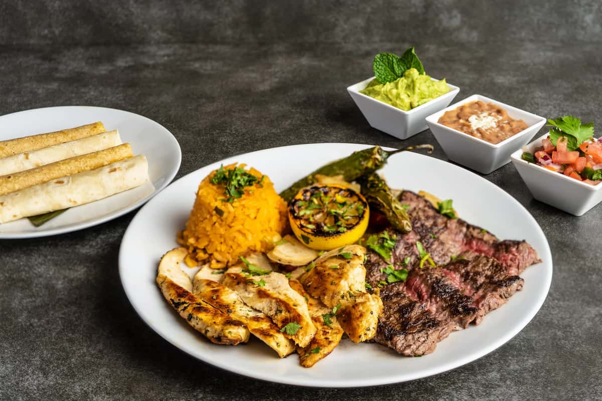Mesero fajita platter with grilled steak, chicken, rice, tortillas, guacamole, beans, and pico.