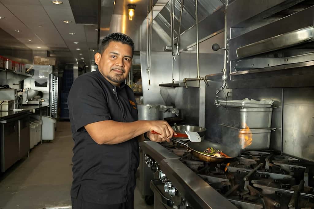 Mesero chef cooking fajitas over an open flame in the restaurant kitchen.
