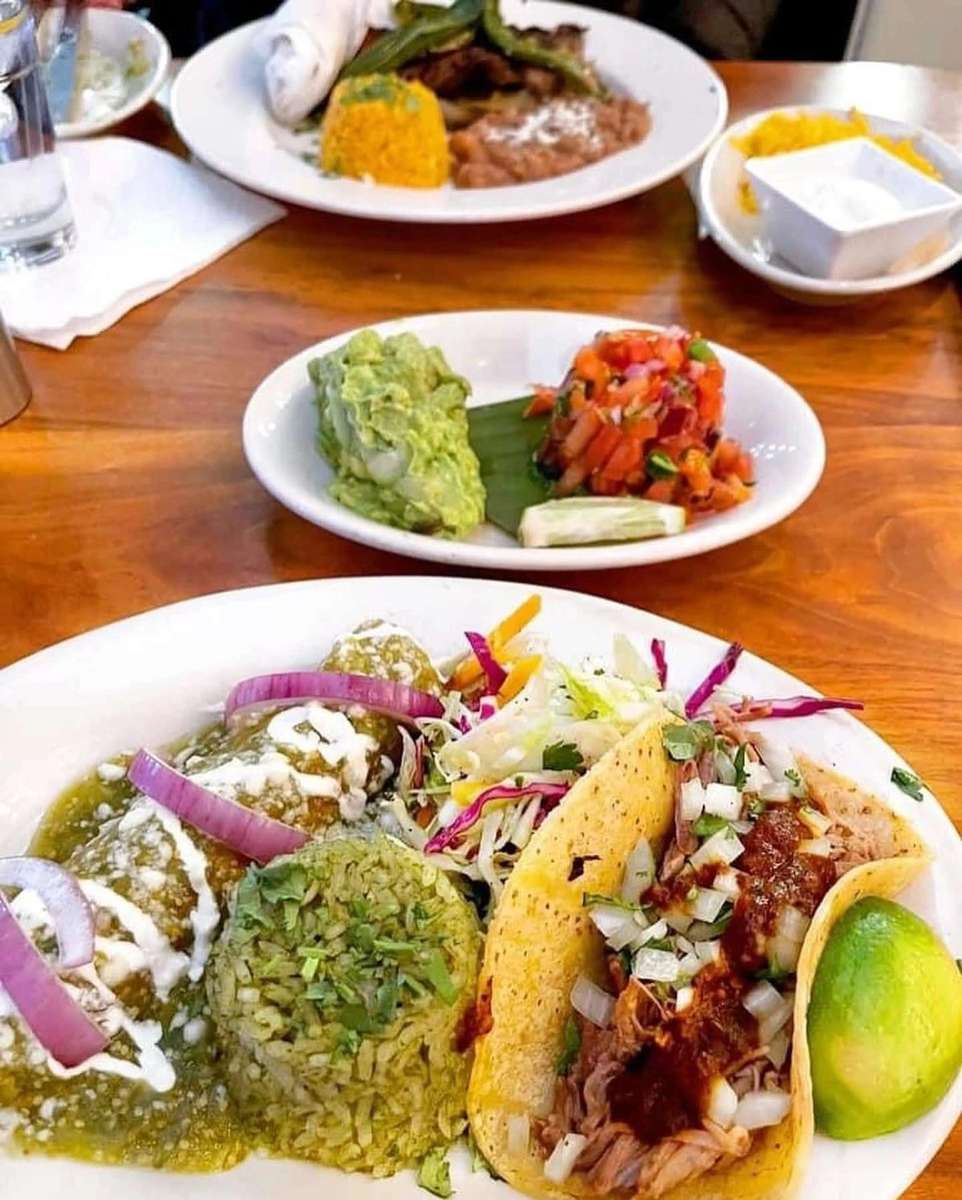 Mexican meal spread with tacos, cilantro rice, guacamole, and roasted vegetables on white plates.