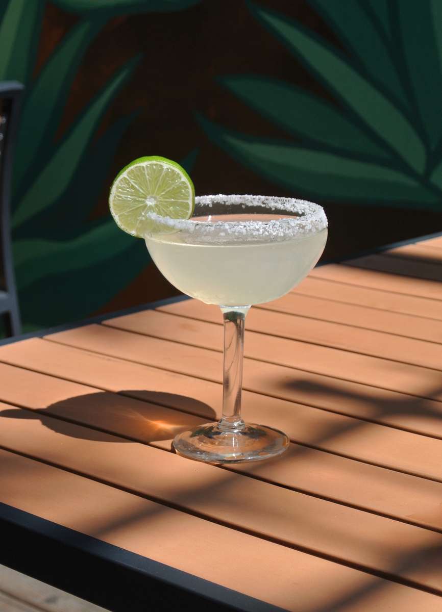 Classic margarita cocktail with lime wheel and salted rim in coupe glass on wooden surface.