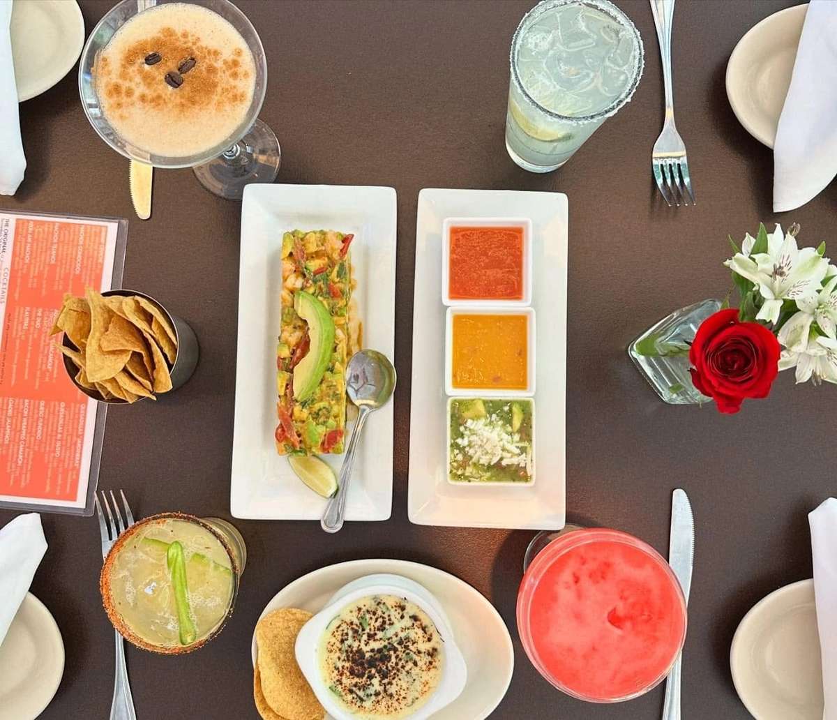 Mesero table spread with chips, dips, Mexican dishes, and colorful cocktails for a celebration.