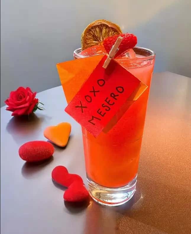 Red Valentine’s cocktail at Mesero with a “XOXO MESERO” tag, garnished with citrus and raspberry, hearts nearby.