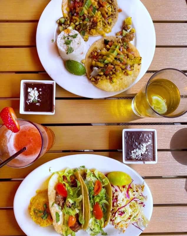 Mesero tacos served with rice, slaw, beans, and drinks on an outdoor table for a bright Tex-Mex meal.