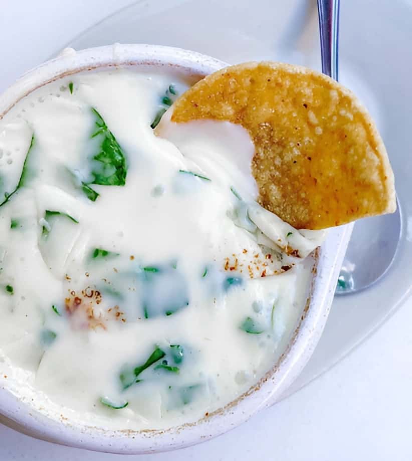 Mesero white queso dip with herbs, served in a warm bowl with a tortilla chip