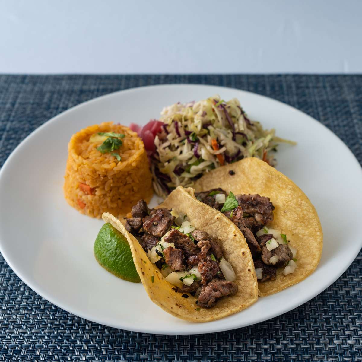 Mesero steak tacos with cilantro and onion, served with Mexican rice, slaw, and fresh lime.