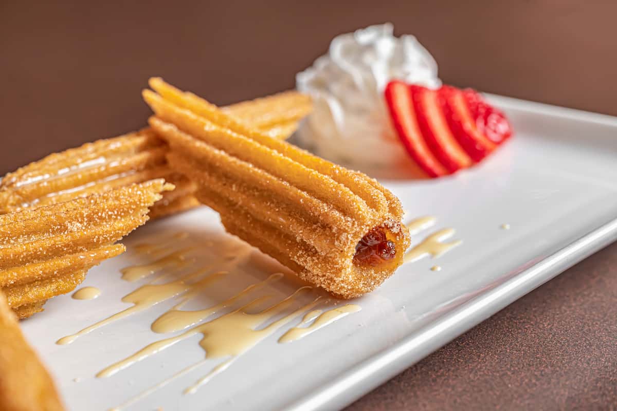 Golden sugared churros served with a sliced strawberry and whipped cream on a white plate.