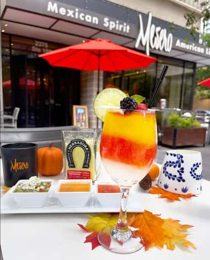 Vibrant layered cocktail garnished with fruit outside Mesero, with salsa trio and Herradura tequila.