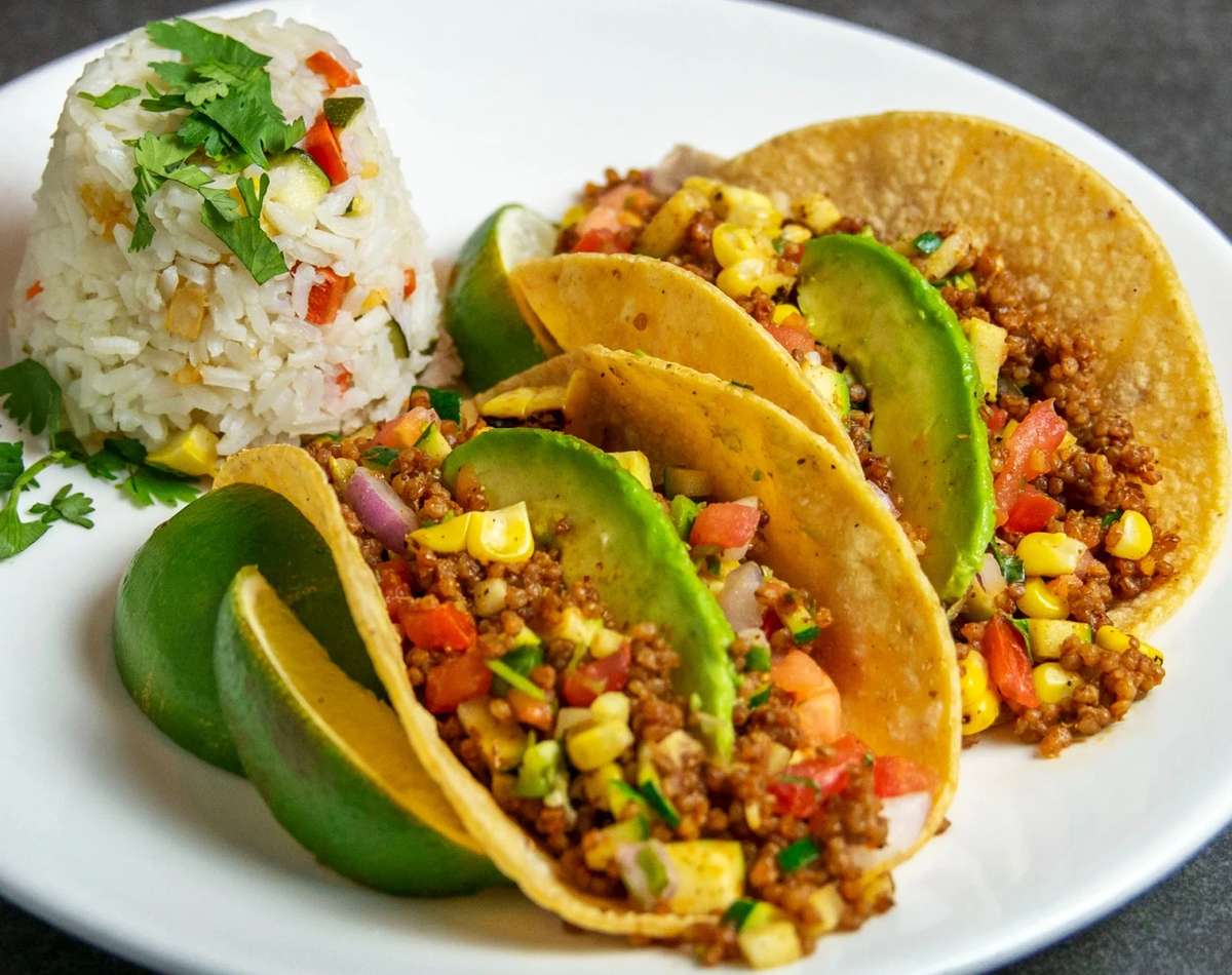 Three veggie tacos with avocado slices and lime wedges, served with a scoop of vegetable rice at Mesero.