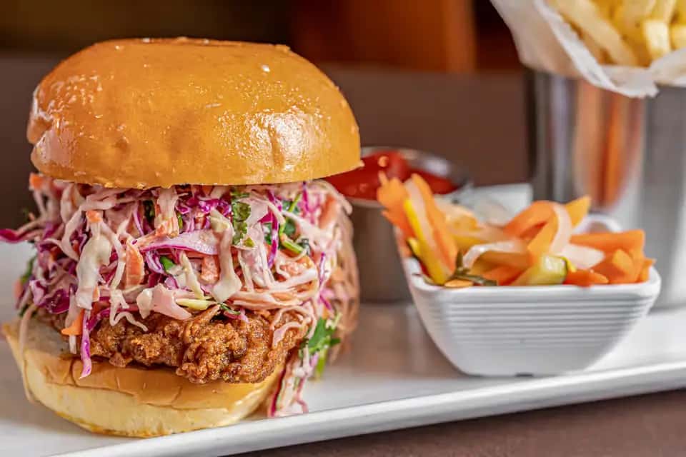 Mesero's crispy chicken sandwich topped with coleslaw, served with fries and pickled veggies.
