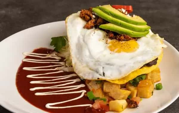Mesero breakfast plate with sunny-side-up egg, avocado slices, chorizo, potatoes, and red sauce drizzle.