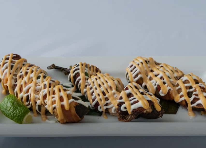 Stuffed and drizzled loaded jalapeños from Mesero, presented on a white platter for festive gatherings.