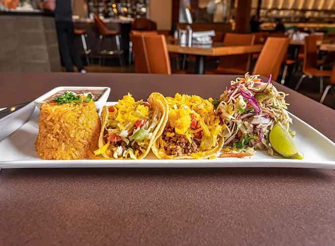 Two brisket tacos are served on a white rectangular plate alongside Mexican rice at Mesero.