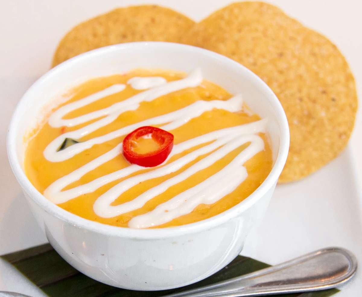 Mesero Queso Tejano topped with crema and red chile, served with crisp tortilla chips.
