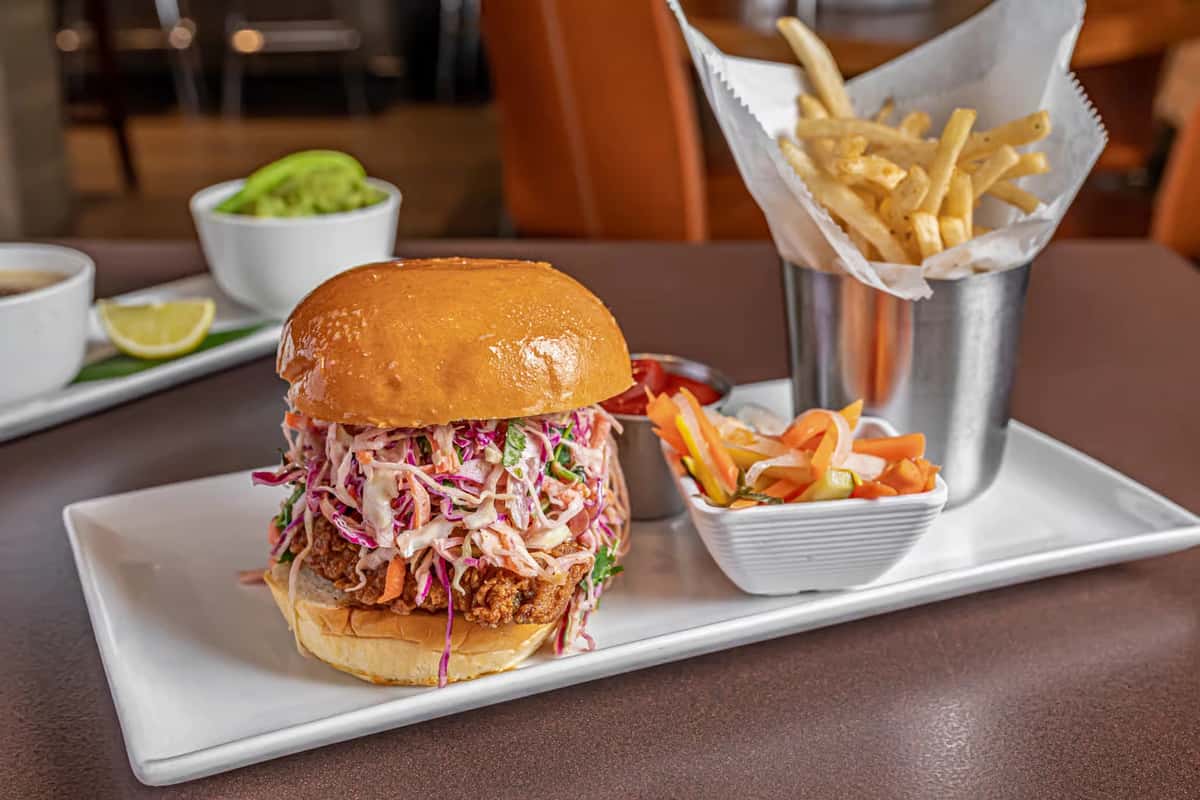 Mesero crispy chicken sandwich topped with purple and white slaw, served next to a cup of French fries.