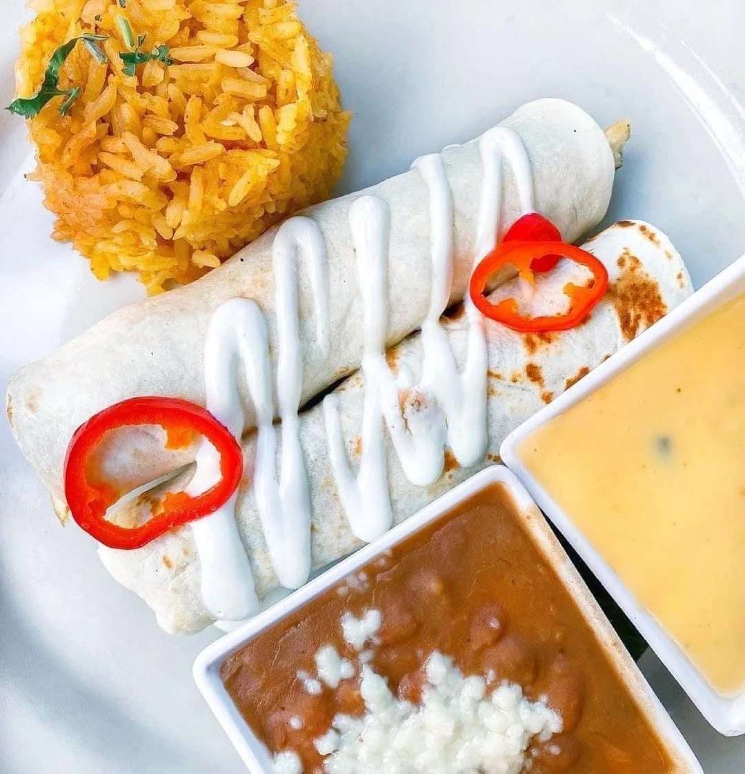 Flour tortillas with filling, yellow rice, and sauces on a white plate at Mesero.