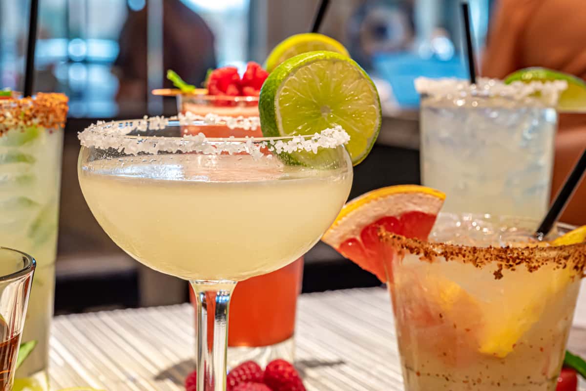 Mesero's margaritas in salt and chilli rims, citrus garnishes, and vibrant cocktails arranged on a bright bar table.