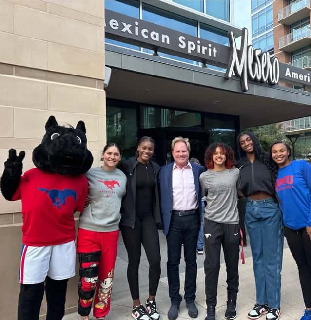 Group visiting Mesero standing together outside the restaurant entrance, celebrating with the SMU mascot.