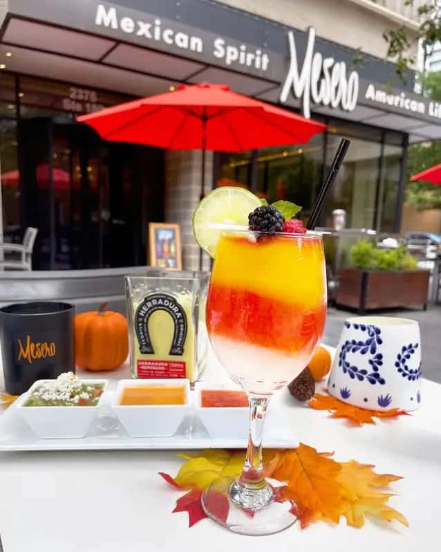 Mesero layered fruit margarita with salsa trio on the patio, set against the restaurant's outdoor signage