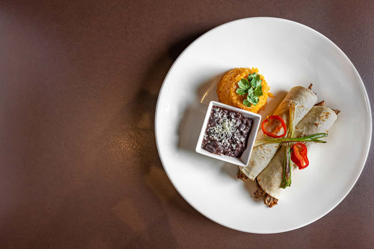 Mesero enchiladas with Mexican rice, black beans, and grilled scallions on a white plate.