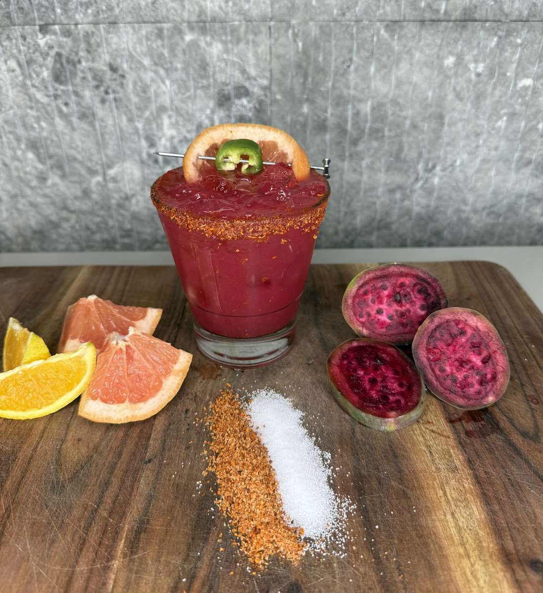 Mesero’s Prickly Pear Paloma with citrus, jalapeño garnish, salt, and spice on a wooden table.