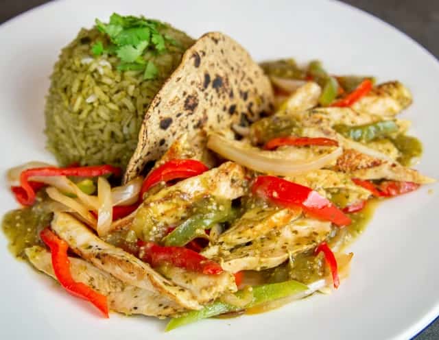 A plate of grilled chicken fajitas with sautéed bell peppers and onions, served with green rice at Mesero. 