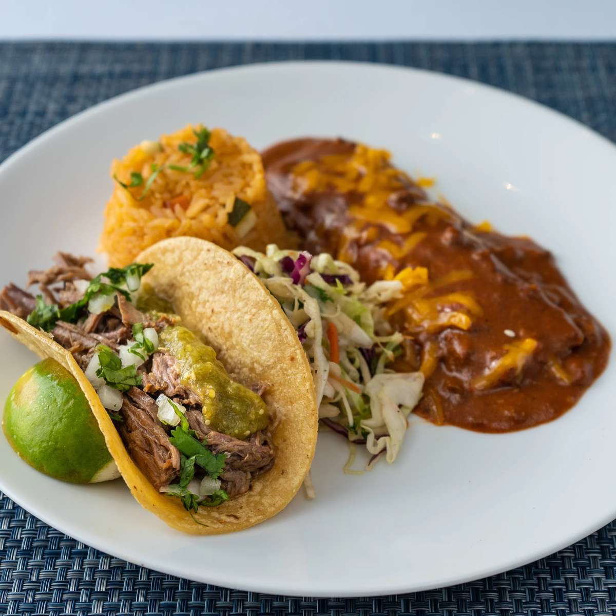 Mesero plate with brisket taco, saucy enchilada, Mexican rice, slaw, and lime.