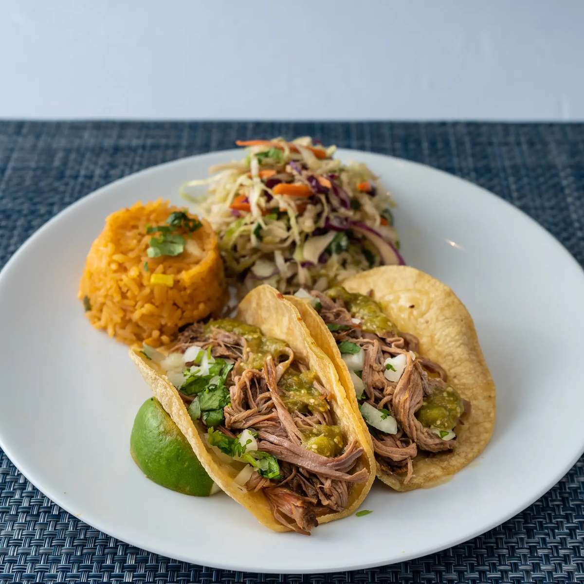 Shredded beef tacos with green salsa, Mexican rice, cabbage slaw, and lime on a white plate