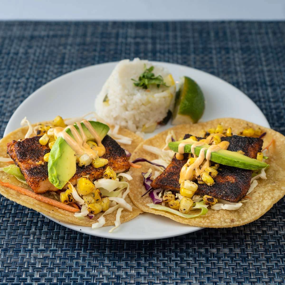 Two blackened fish tacos with corn, cabbage, and avocado, served with white rice.