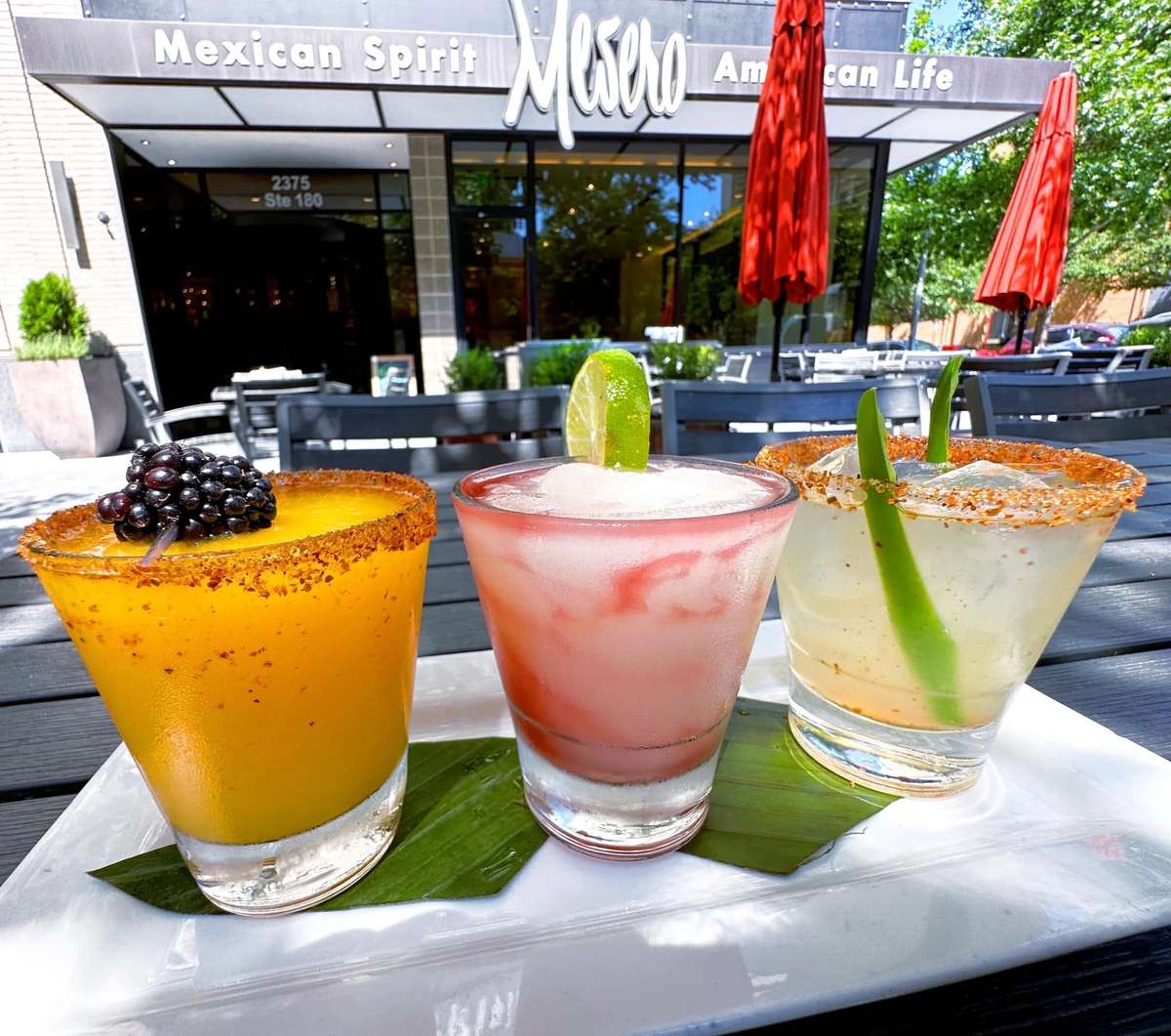 Mesero margaritas served on a patio table with colorful fruit garnishes.