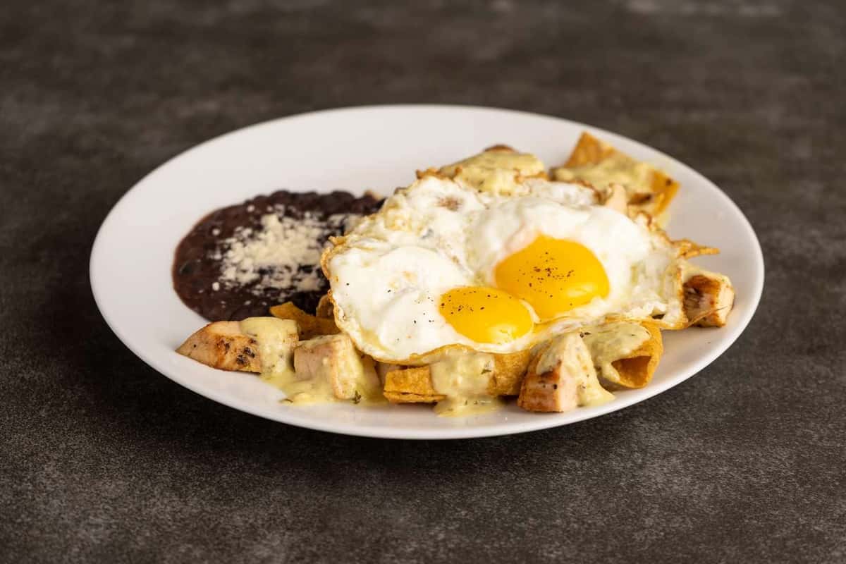 Breakfast plate with fried eggs, black beans, potatoes, and tortilla chips on a white plate at Mesero.