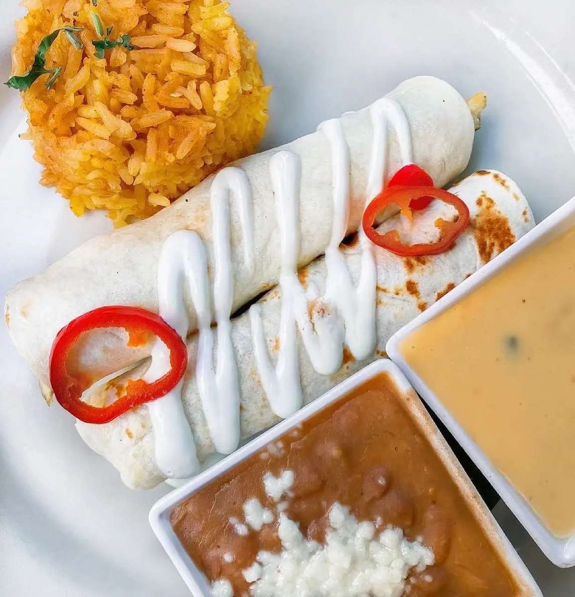Two enchiladas topped with red chillies, served with Mexican rice, beans topped with cheese, and queso dip at Mesero.