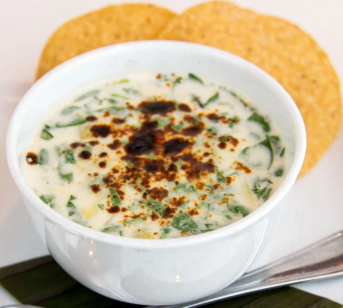 Creamy Mexican soup garnished with herbs and chili seasoning, served with crispy tortilla chips.