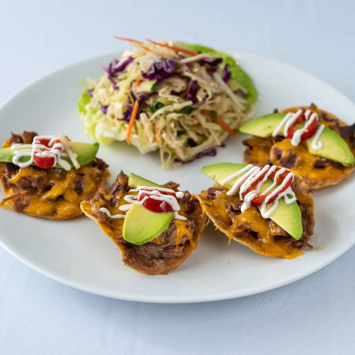 Mesero shared bites topped with beef, cheese, avocado, tomato, and crema beside fresh slaw.