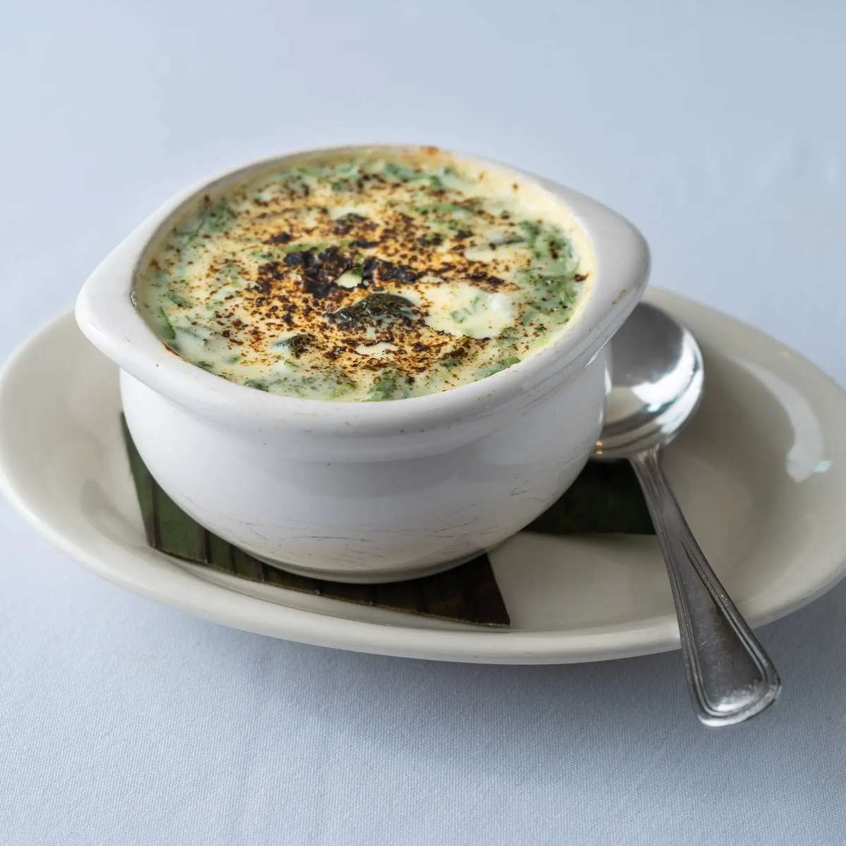 Mesero's creamy spinach and cheese queso served in a white bowl with a spoon on a plate.