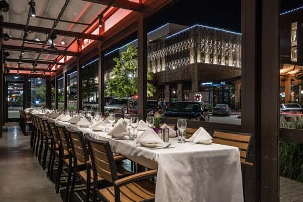 Elegant outdoor dining setup at Mesero, overlooking a modern shopping plaza at night.