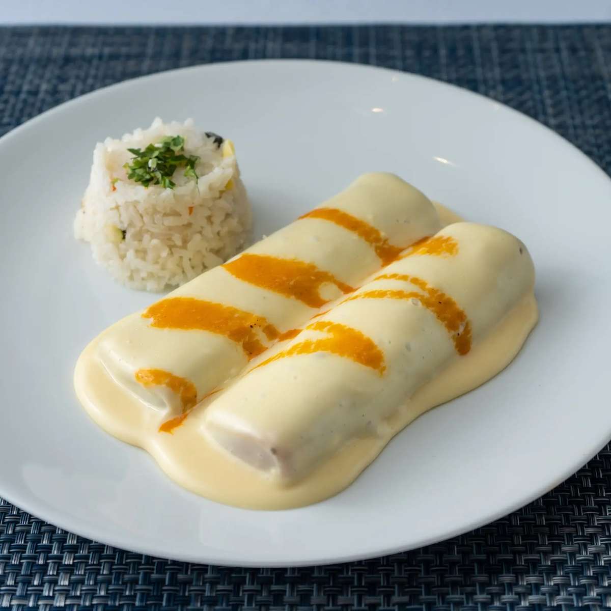 Mesero enchiladas covered in creamy cheese sauce with orange drizzle, served with a side of white rice.