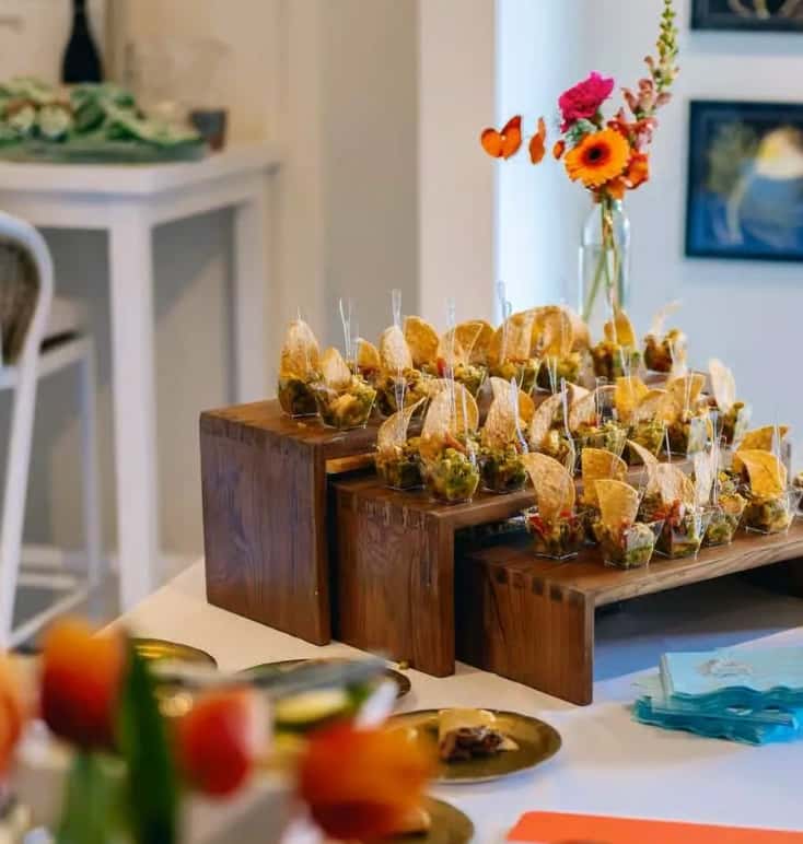 Mesero catering display with mini chips and dip cups arranged on wooden risers for a festive event setup.